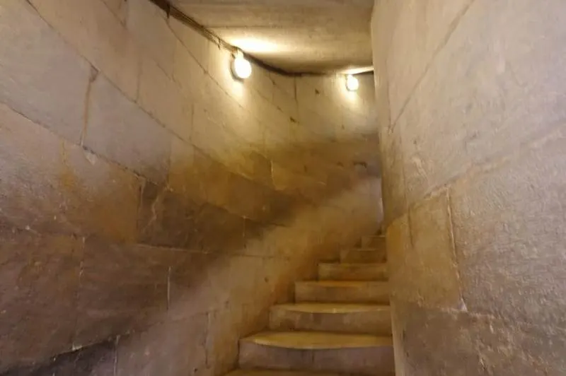 Narrow winding staircase with pale stone steps and walls