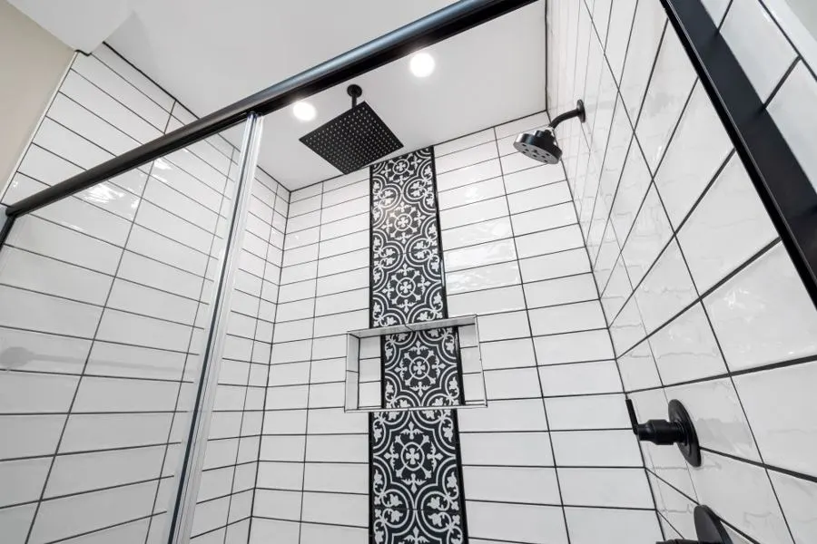 White tiled shower with a decorative strip and black overhead shower