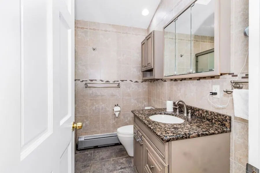 Bathroom with pale stone tiles, a bathtub and a granite-topped vanity