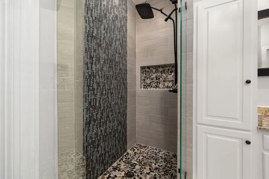 Grey mosaic shower strip between pale tiled walls