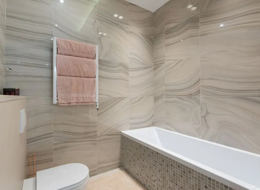 Bathroom with flowing marble-pattern wall tiles and a white bathtub